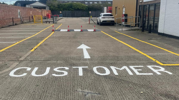 Line marking team applying MMA pedestrian walkway at industrial site.