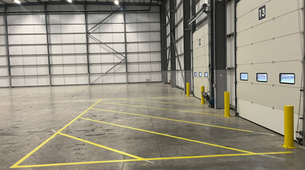 Green fire escape route markings and yellow safety zones inside a distribution warehouse.